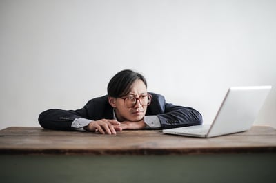 Confused man leaning on desk looking at laptop